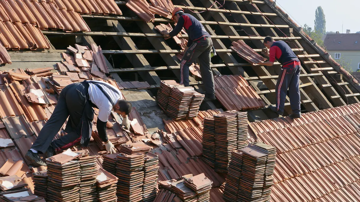 Muncitori demontând învelitoarea de țiglă a unui acoperiș pe zone, în timpul decopertării