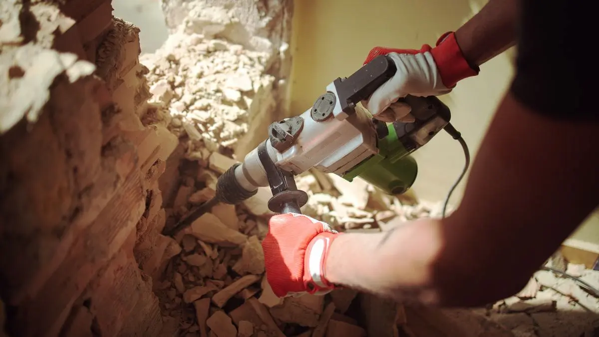 Muncitor care demolează controlat un perete interior cu ciocan demolator